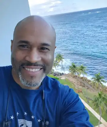 Jean Nicolas smiling on a balcony above the ocean and palm trees